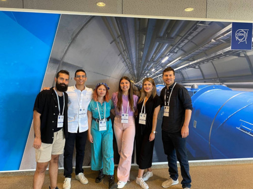 Six people stand in front of CERN backdrop. Poppy Silk is the person in the centre. All wear lanyards.